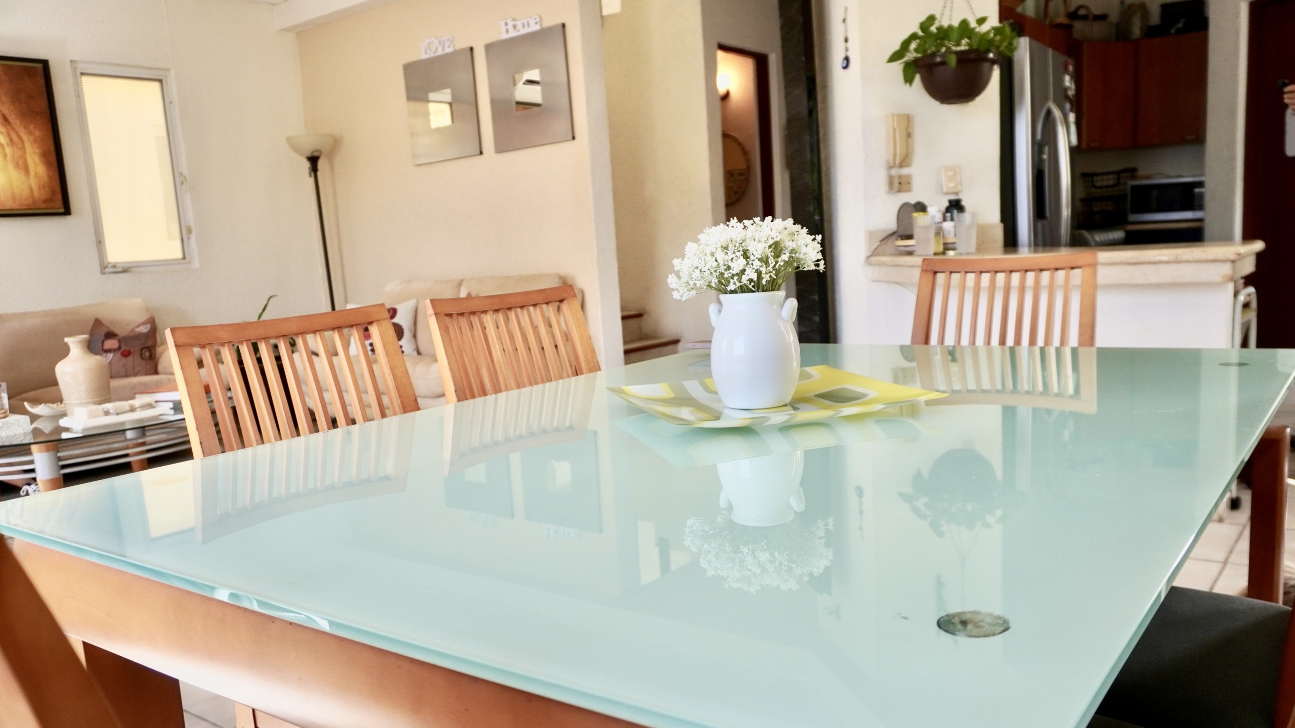 Departamento en venta en centro cancún - Comedor con mesa de cristal y sillas de madera. Al fondo una sala de estar